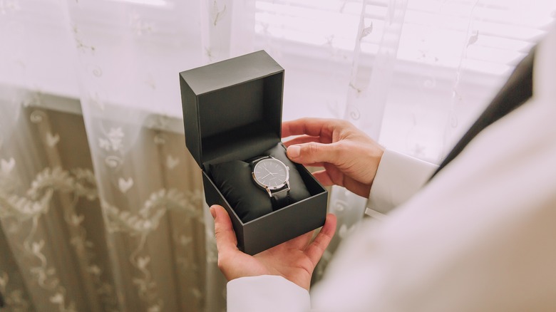 A man holding an open gift box with a luxury watch inside.