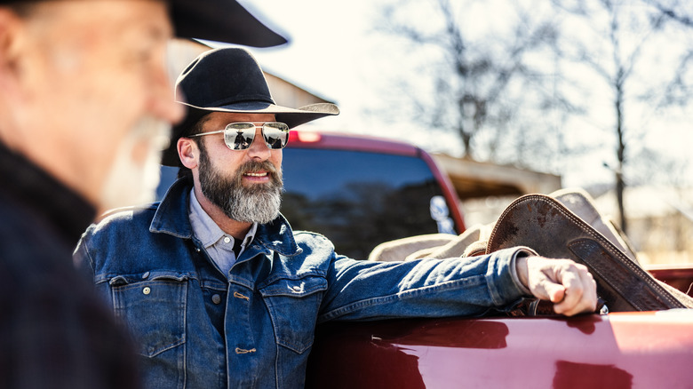 Cowboy in sunglasses and hat leaning against back of truck