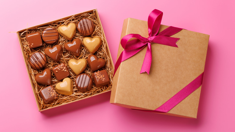 A charming box of chocolates, open to show a variety, against a pink background.