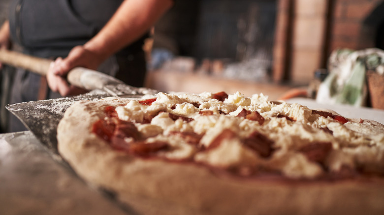 An uncooked pizza being placed into an oven