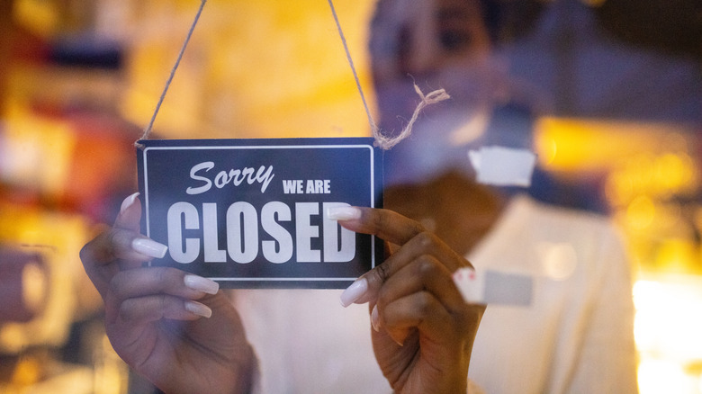Woman putting closed sign on glass front door of coffee shop