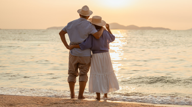 A retired couple standing together and enjoying a sunny day by the ocean