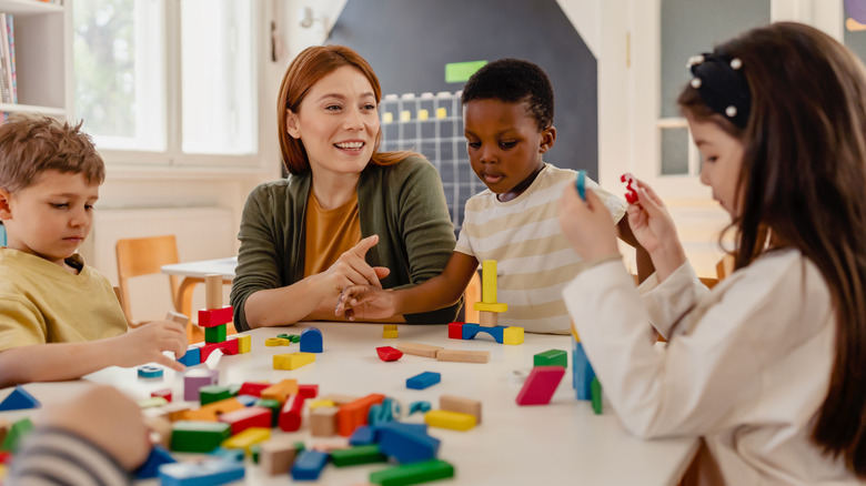 Preschool children play with colorful blocks at a table under the smiling gaze of a teacher