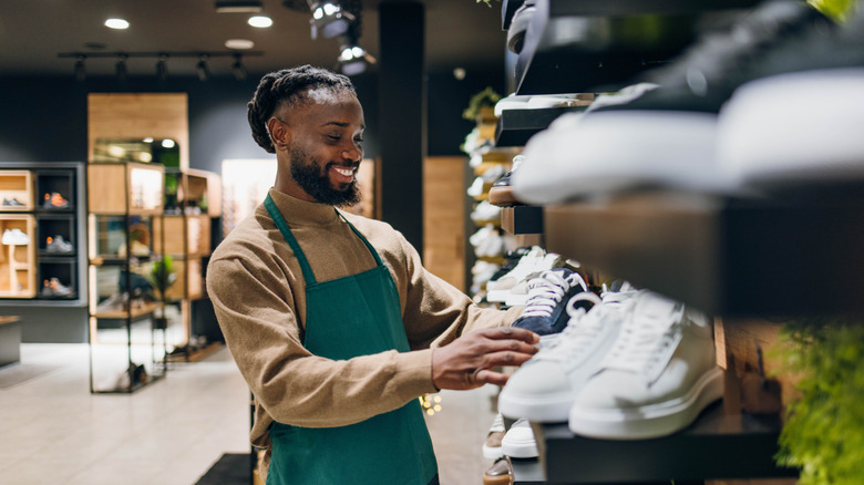 A young salesman smiling as he stocks the shelves at a shoe store