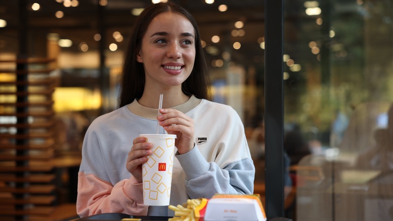A smiling Gen Z woman sitting in McDonalds while holding a drink.