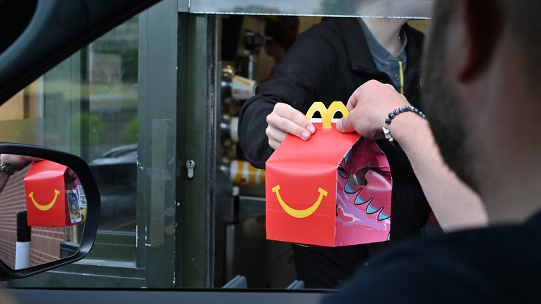 A man at a drive-thru window picking up a McDonald's Happy Meal.