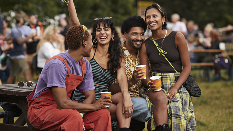 Happy couples sitting with drinks in disposable cups at music festival