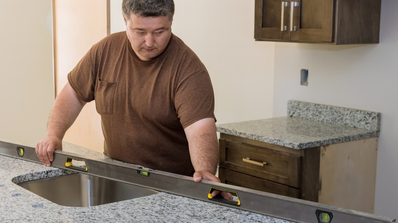 Worker checking the level of a granite kitchen island countertop with a sink cutout during installation