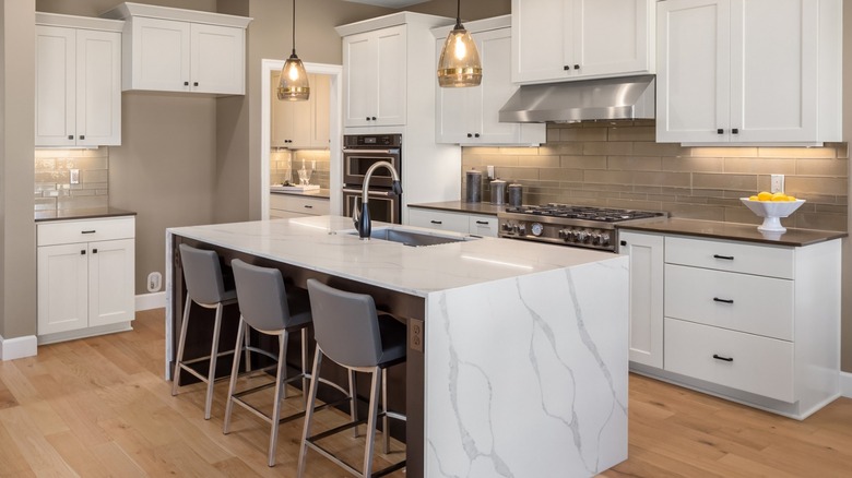 Modern kitchen with white cabinets, a large marble-look island with seating, pendant lights, stainless steel appliances, and wood flooring