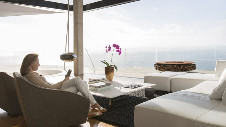 Woman sitting down with a smarphone in a luxury home facing the sea