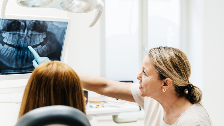 white female dentist points to X-ray while talking to female patient who shows only the back of her head