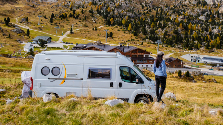 White van in the mountains with woman standing outside