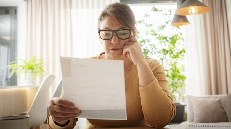 A woman looking stressed reading a bill while sitting at a table.