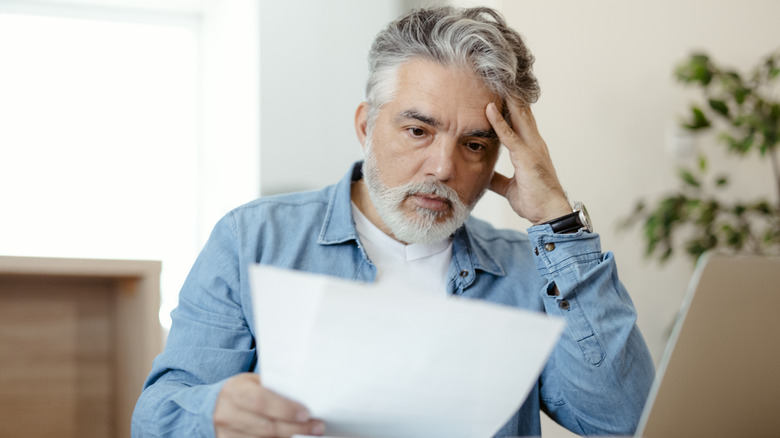 A concerned senior man reading a document in front of a laptop.