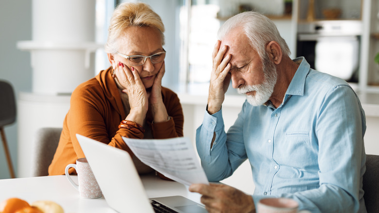 A stressed mature couple reading a letter in front of a laptop