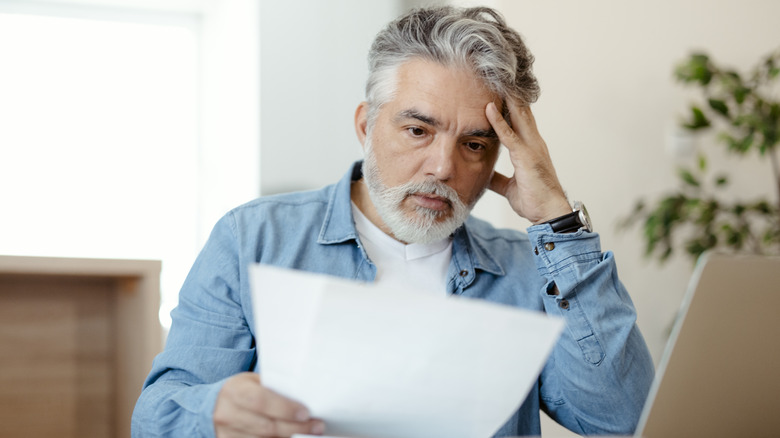 A concerned senior man reading a document in front of a laptop.