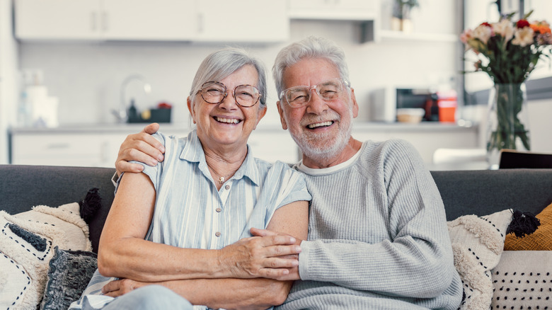A smiling elderly couple sitting together on a couch.
