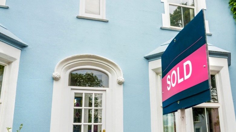 A SOLD sign in front of a blue house.