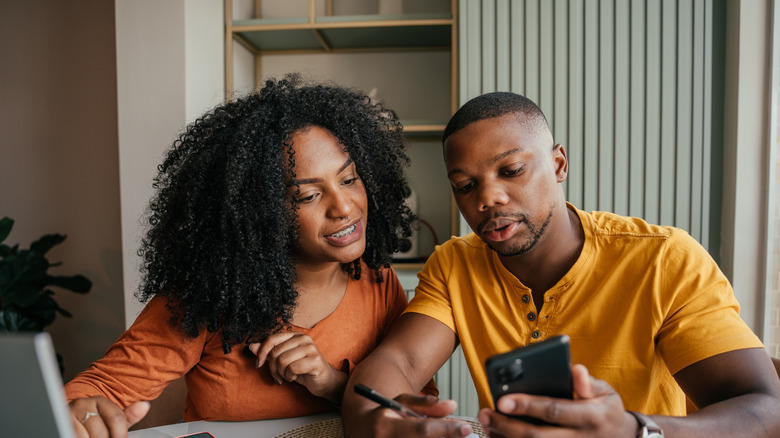 Young couple looking at their phone; the man has a pen