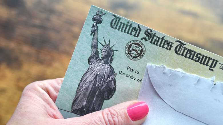 A woman's hand holding a check from the U.S. Treasury and a torn envelope