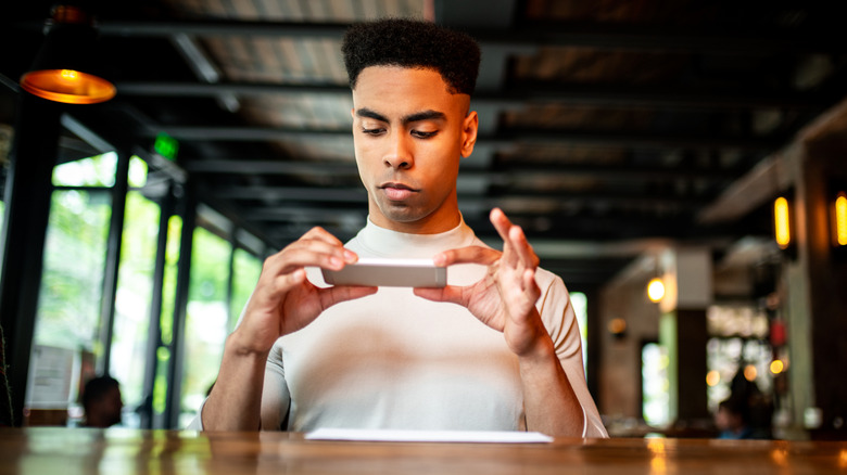 A young man uses his phone to deposit a check