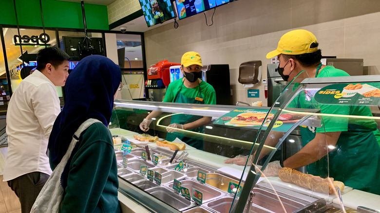 The interior of a Subway location with employees making sandwiches for customers