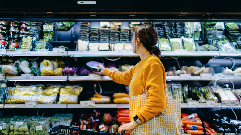 Young Asian woman with shopping cart, carrying a reusable shopping bag.