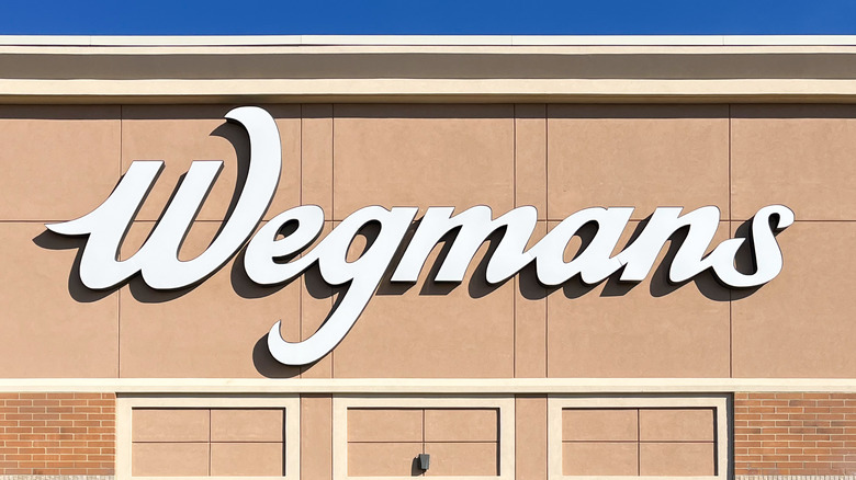 A white car is parked in front of a Wegmans store.