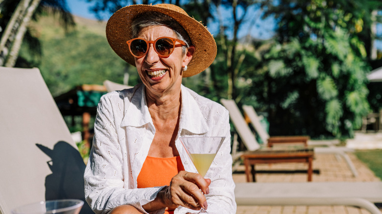 A smiling mature woman on lounge chair holding a cocktail.