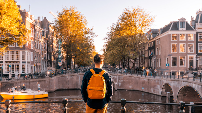A Gen Z man wearing a backpack looking out over a canal in Europe.