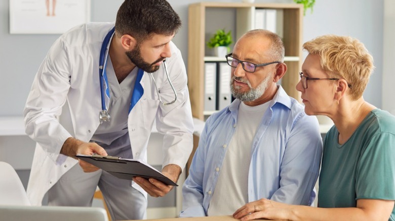 A medical professional explaining something to an older middle aged couple nearing retirement.