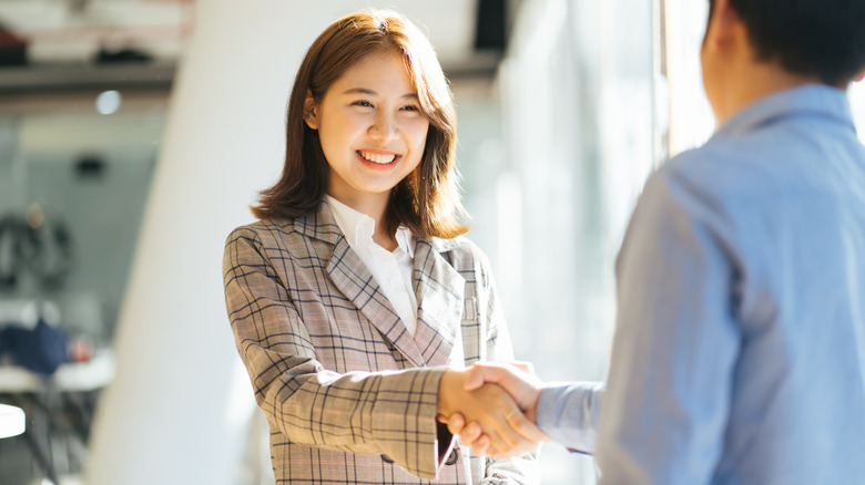 Young woman shaking someone's hand in an office.