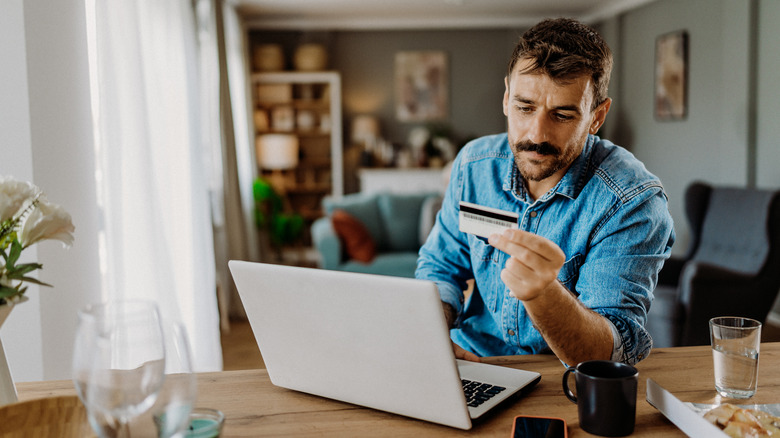 Man looking at credit card while sitting at table with computer