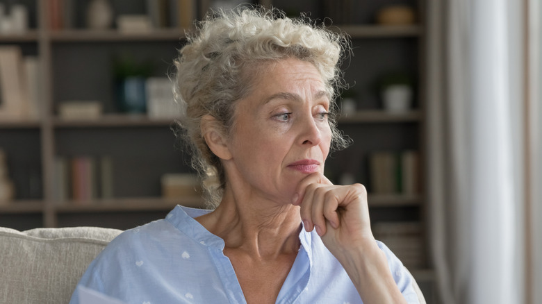 Doubtful senior woman retiree sit on sofa hold business finance document