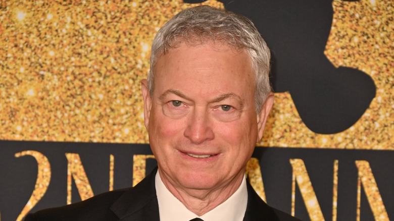 Gary Sinise on the red carpet in front of a gold and black sign
