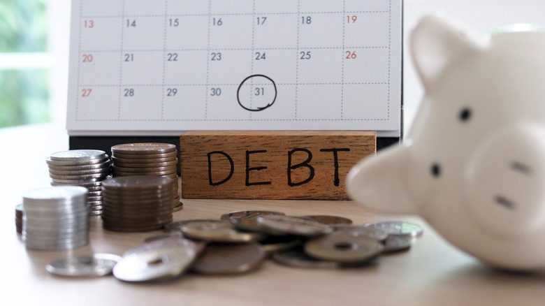 piggy bank on its side, a stack of coins, a calendar with a deadline circled, and block labeled "Debt"