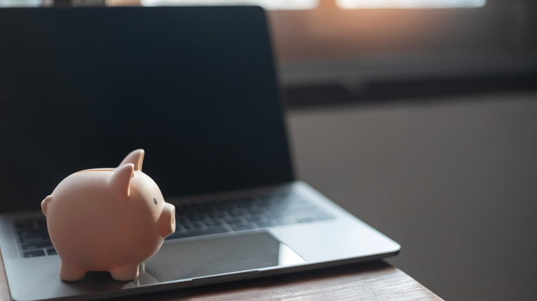 A pink piggy bank sitting on a laptop.