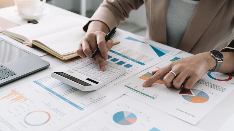 A financial analyst looking at graphs and doing math with a calculator