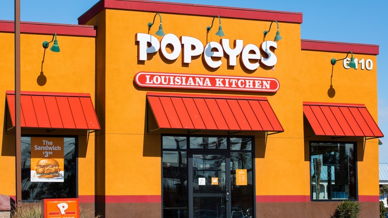 Exterior of a Popeyes Louisiana Kitchen restaurant with orange walls, red awnings and the chain's large white-and-red sign above the entrance