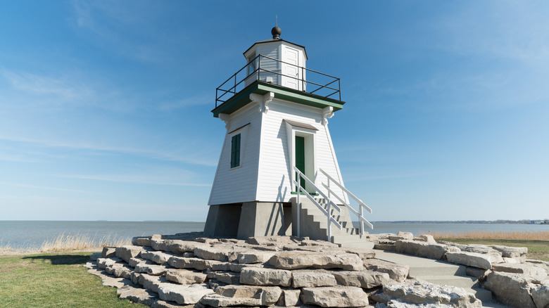 A white lighthouse on a rock foundation in Port Clinton with blue skies and Lake Erie in the background.