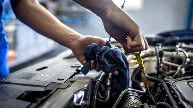 A techniciam checking the oil on a vehicle by pulling up the dip stick with one hand and holding a blue cloth in the other hand.