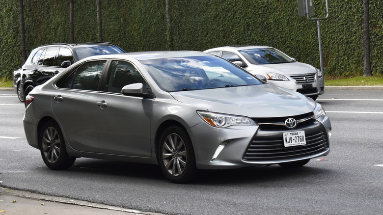 Toyota Camry, a high-end grey luxury sedan captured in motion along an urban roadway,.
