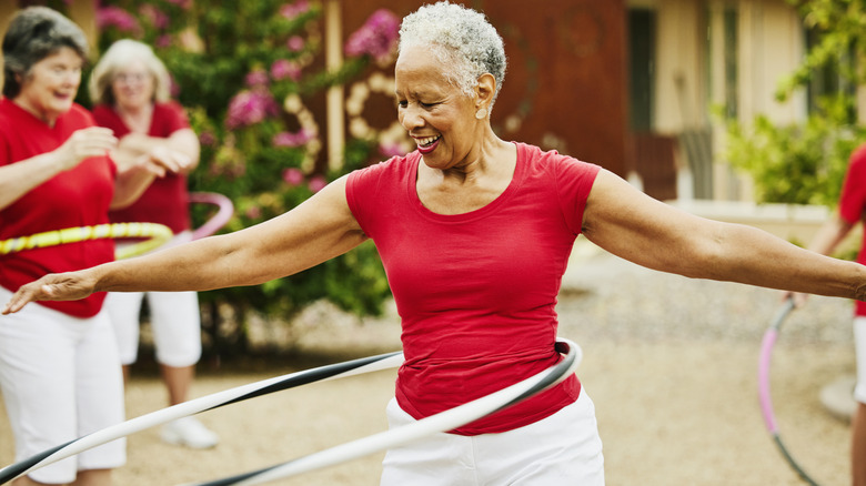 A group of mature women smiling while hula hooping in a courtyard.