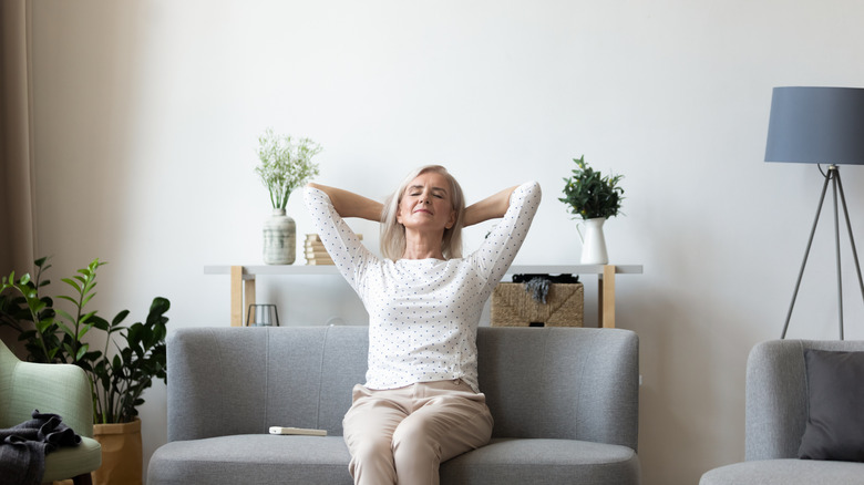 A relaxed mature woman sitting on a sofa with her hands behind her head.