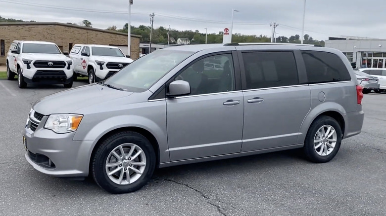 A silver 2020 Dodge Grand Caravan SXT parked outside a dealership with trucks and sedans behind it