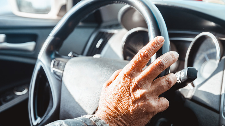 A mature hand holding a steering wheel.