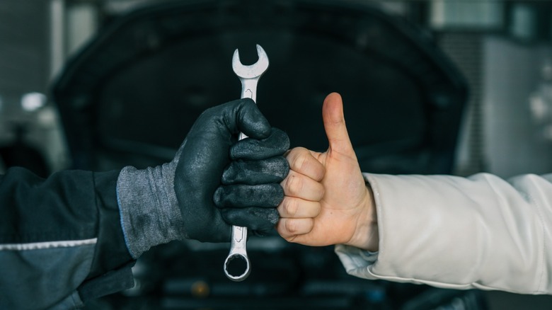 a gloved hand holding a wrench fist bumps an ungloved hand