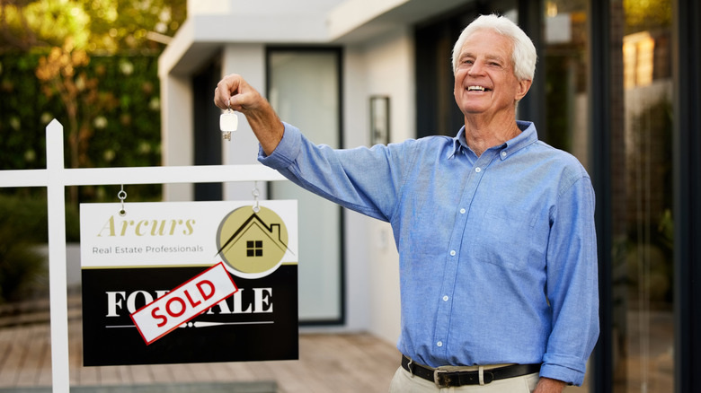 mature man standing with sold house sign