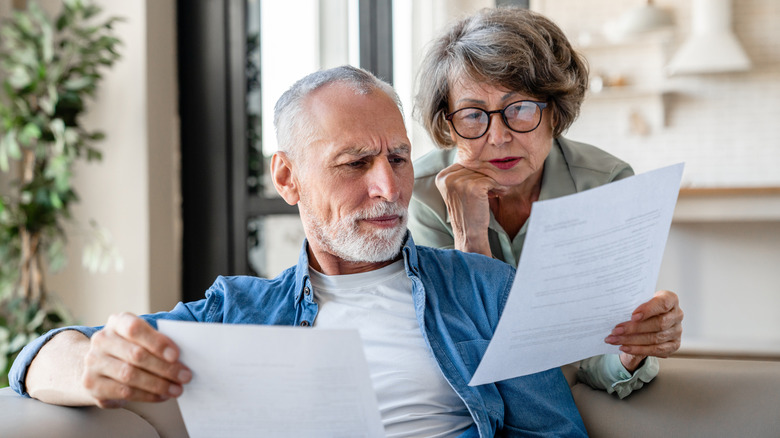 A mature couple scrutinizing two different documents in their living room.