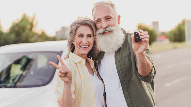 A mature couple hugging while holding up a peace sign and a car keys